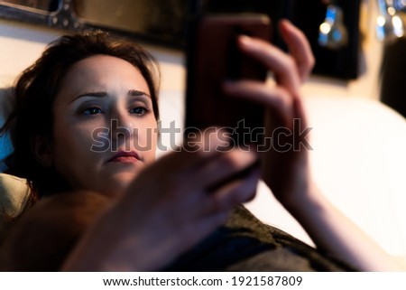 beautiful middle-aged woman looking at the smart phone lying on a couch at home tired carrying her baby at night.