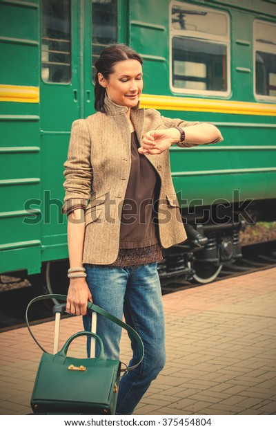 beautiful middle-aged woman with luggage standing\
near a railway car and looks at his watch. Instagram image filter\
retro style