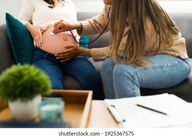 Beautiful midwife using a stethoscope in the naked belly of an expectant mother. Latin doula checking the health of a woman and her baby