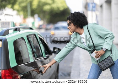 Beautiful millennial african american young lady wearing smart casual outfit with smartphone and takeaway coffee in her hand taking taxi on street, corporate businesswoman going to office