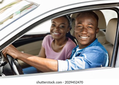 Beautiful Millennial Afro American Couple Posing In Their New Auto, Cheerfully Smiling At Camera While Making Test Drive, Side View, Closeup. Happy Black Man And Woman Going Summer Vacation By Car