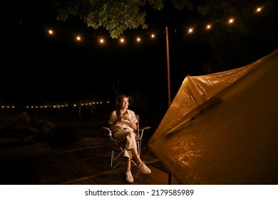 Beautiful Millennial Asian Female Relaxes Sipping Hot Cocoa Or Coffee While Looking At The Beautiful Sky At Night In The Campground.