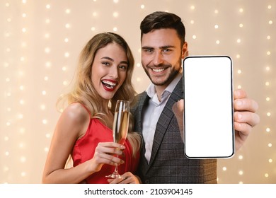 Beautiful Millennial Couple In Nice Outfits Posing At Restaurant, Drinking Champagne, Celebrating Anniversary, Hugging And Showing Cellphone With Empty Screen, Dating Mobile App, Mockup