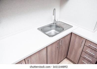 A beautiful and minimalistic workplace for a housewife. Aluminum sink with tap fitting in the corner of the kitchen worktop. Design and interior of a compact kitchen.