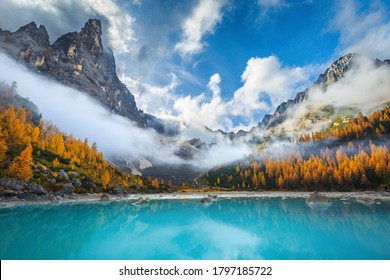 Beautiful misty mountains and colorful yellow larches on the shore of the lake Sorapis. Breathtaking autumn scenery in the Dolomites, Italy, Europe