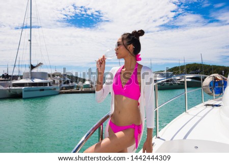 Beautiful Mix Race Tanned skin Woman drink Wine glass along Luxury Yachts in Marina Bay Club, pink bikini swim suit post as Fashion Model in docking pier under summer blue sky in vacation holiday