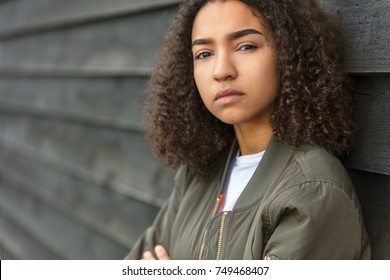 Beautiful mixed race biracial African American girl teenager female young woman outside wearing a green bomber jacket looking sad depressed or thoughtful