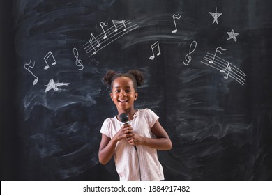 Beautiful Mixed Race Elementary School Girl Standing In Front Of A Chalkboard In Classroom, Singing While In Music Class With Musical Note Symbols Drawn On The Blackboard