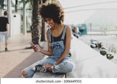 beautiful mixed race girl with afro hair listening to her favorite music through headphones using a mobile phone. an attractive black young woman adds a new track to her playlist using a mobile app - Powered by Shutterstock