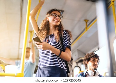 Beautiful mixed race girl with long curly hair using smart phone for reading or writing message while standing in city bus.