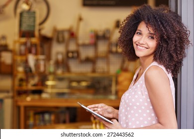 Beautiful mixed race woman with an afro hairstyle holding a digital tablet while standing in the doorway of her coffee shop  - Powered by Shutterstock