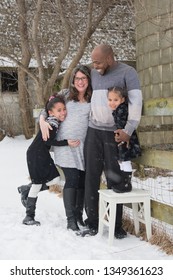 A Beautiful Mixed-race Family (African American And Filipino/Caucasian) Poses Outside On A Snowy Winters Day. Relaxed, Happy Expressions And Smiles Convey Closeness And Love. Rural Farm Background.