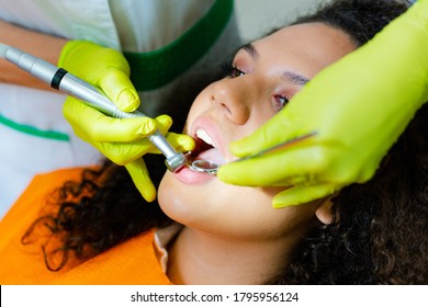 Beautiful mixed-race teenage girl  having tooth drill procedure at dental office. Hands in green protective gloves holding instruments. 