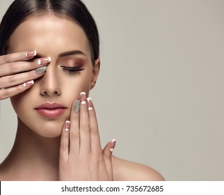 Beautiful model girl with a beige French manicure nail design with rhinestones . Fashion makeup and care for hands and nails and cosmetics .
