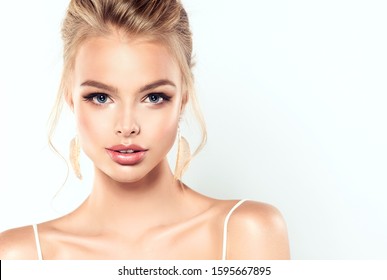 Beautiful Model Girl With Blond Hair . Woman With A High Hairstyle Is Wearing A White Top.Fashion Makeup And Cosmetics . Big Golden Shine  Earrings Jewelry .