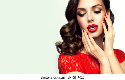 Beautiful    Model  Girl  With Curly Brown  Hair . Brunette Woman With Wavy Hairstyle  . Red  Lips ,dress And  Nails Manicure .    Fashion , Beauty And Make Up Portrait