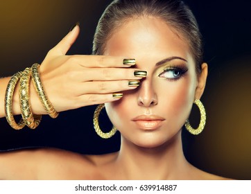 Beautiful Model Girl With  Golden Makeup And Gold  Metal Manicure  Nails.  Fashion Woman Portrait . Jewelry, Earrings And Bracelets .