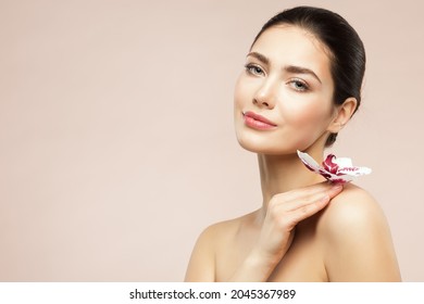 Beautiful Model Girl Holding Orchid Flower On Shoulder. Beauty Woman With Perfect Healthy Skin And Natural Makeup. Body And Face Care Cosmetics