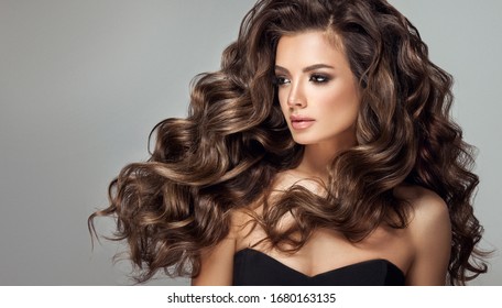 Beautiful model girl with long wavy and shiny hair . Brunette woman with curly hairstyle