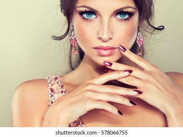 Beautiful model girl with pink metallic manicure on nails . Fashion makeup and cosmetics . Pink dress with rhinestones and pink earrings jewelry .