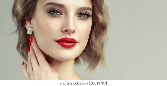Beautiful model girl with short curly  hair and red lips . Red manicure on nails .Beauty and esthetic care . Modern styling for blonde haired. Earrings jewelry and accessories
