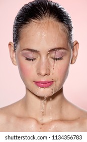 Beautiful Model Girl with splashes of water on her face. Beautiful Woman under splash of water with fresh skin over pink background. Skin care Cleansing and moisturizing concept. Beauty face