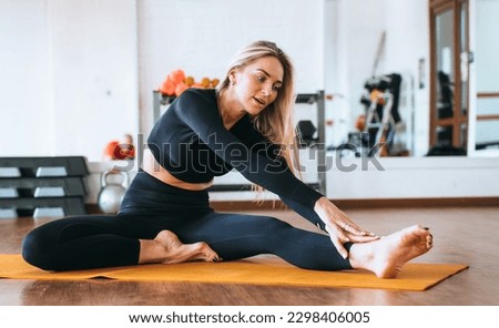 Beautiful model makes stretching exercise in yoga mat at fitness club. Fit caucasian young woman warms up on sandy morning. Healthy women, flexibility. Focused female training. Leisure activities.