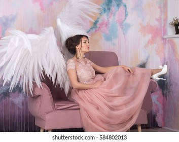 beautiful model with open angel wings  sitting on the sofa with pink sky background