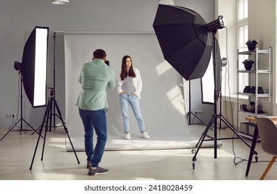 Beautiful model posing for male photographer in studio. Rare view of photographer taking pictures of female model with digital camera in photo studio with professional photographic equipment - Powered by Shutterstock