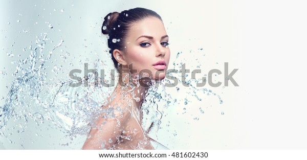 Beautiful Model Spa Woman with splashes of water.\
Beautiful Smiling girl under splash of water with fresh skin over\
blue background. Skin care, Cleansing and moisturizing concept.\
Beauty face