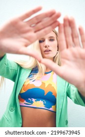 Beautiful Model, A Triangle Sign With Fashion Hands Looking Though It In Bright, Colorful Clothes. Portrait Of A Young Beautiful Woman With Artistic, Trendy And Funky Style Standing Outdoors.