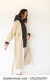 Beautiful Model Turn Around. Sensual Brunette Wear Minimalistic Outfit. Young Woman In Beige Trench Coat, Grey Hoody And White Pants. Winter, Fall Autumn Or Spring Minimal Outfit. Woman Look Elegant.