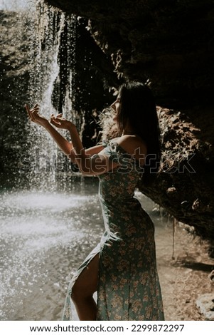 Beautiful model in a turquoise dress posing near a mountain waterfall.Wildlife concept