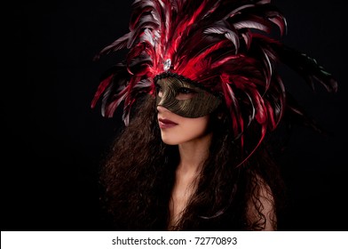 Beautiful Model Wearing A Red Feather Mask Symbolizing Mardi Gras Or Venetian Carnival Over Black Background