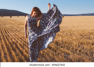 Beautiful model wearing summer cotton maxi dress and jewelery posing in autumn field with hay stack. Boho style clothing and jewelry.