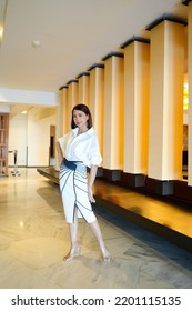 Beautiful Model Woman In White Dress In Modern Corporate Building Lobby.