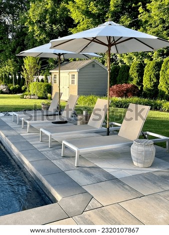 Beautiful, modern backyard lounge area with concrete umbrella stand poolside, next to a charcoal pool's tanning sundeck on top of gray stone pavers. Inspired by Tulum, Mexico's eco-chic feel.