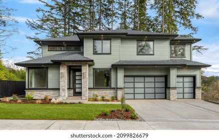 Beautiful Modern Luxury Home Exterior. Features Three Car Garage, Two Stories, Stone Accents Around Entrance And Lower Portion Of House. Backdrop Of Trees And Blue Sky.