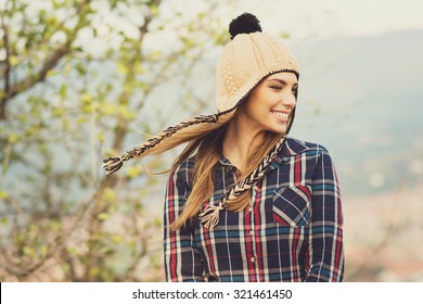 Beautiful modern urban young woman wearing blue and red plaid shirt and knitted beige and black hat. Trendy teenage girl in autumn outdoors. Horizontal, medium retouch, matte filter.