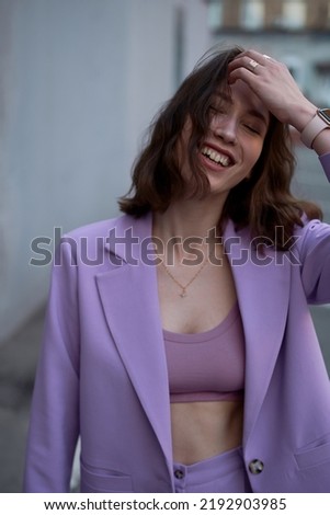 Beautiful modern woman in parking area. Fashionable. Violet suit. Yellow top. Brown hair. European type. Slim and tall. Daily life. Work and leisure. City background. Soft light.
