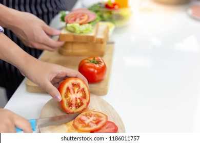 Beautiful Mom Is Chopping Tomato By Using Knife On Cutting Board At Kitchen For Making Sandwiches To Her Children In The Morning With Her Husband Before Child Go To School. Tomato Is Good For Health