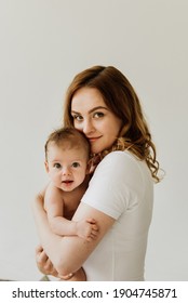 Beautiful mom hugs and kisses the newborn in the studio on a white background. A young mother in a white bodysuit hugs and kisses her newborn daughter in the studio. - Shutterstock ID 1904745871