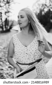 Beautiful Mom In The Park, In A Summer Dress. Loose Hair And Open Arms. Summer Walk. Portrait Of Mom.