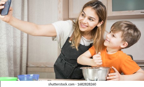 Beautiful Mom And Son Cooking And Making Selfie At Home. Happy Family Having A Facetime Video Call. Unity, Connection, Home Education Concept.