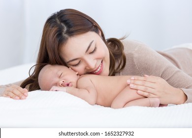 Beautiful Mom Supports And Tenderly Cuddles The Newborn Baby Gently While The Infant Is Sleeping. Asian Mother Using Her Cheek Touching On The Back Of Babies, Looking With Love And Care.