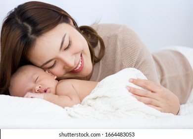 Beautiful Mom Supports And Tenderly Cuddles The Newborn Baby Gently While The Infant Is Sleeping. Asian Mother Using Her Cheek Touching On The Back Of Babies, Looking With Love And Care.