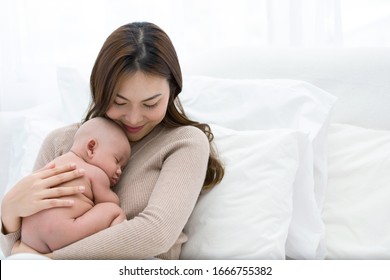 Beautiful Mom Supports And Tenderly Cuddles The Newborn Baby Gently While The Infant Is Sleeping On The Chest. Asian Mother Looking At The Baby With Love And Showing Protection.