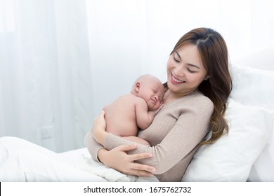 Beautiful Mom Supports And Tenderly Cuddles The Newborn Baby Gently While The Infant Is Sleeping On The Chest. Asian Mother Looking At The Baby With Love And Showing Protection.