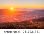 Beautiful morning cityscape. View from the mountain to the city at sunrise. The sun rises over the sea bay and mountains. Travel and tourism in the Magadan region. City of Magadan, Far East of Russia.