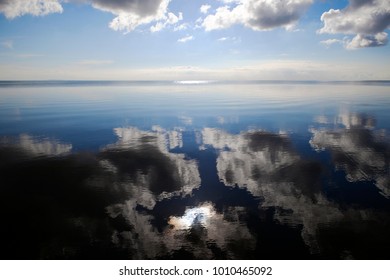 Beautiful Morning Clouds In Blue Sky With Reflection In Calm Water With Sun Glare In Foreground . Nature Wallpaper